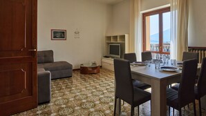 Une pièce comprenant une table à manger, des chaises, un canapé, un téléviseur et une fenêtre avec des rideaux.