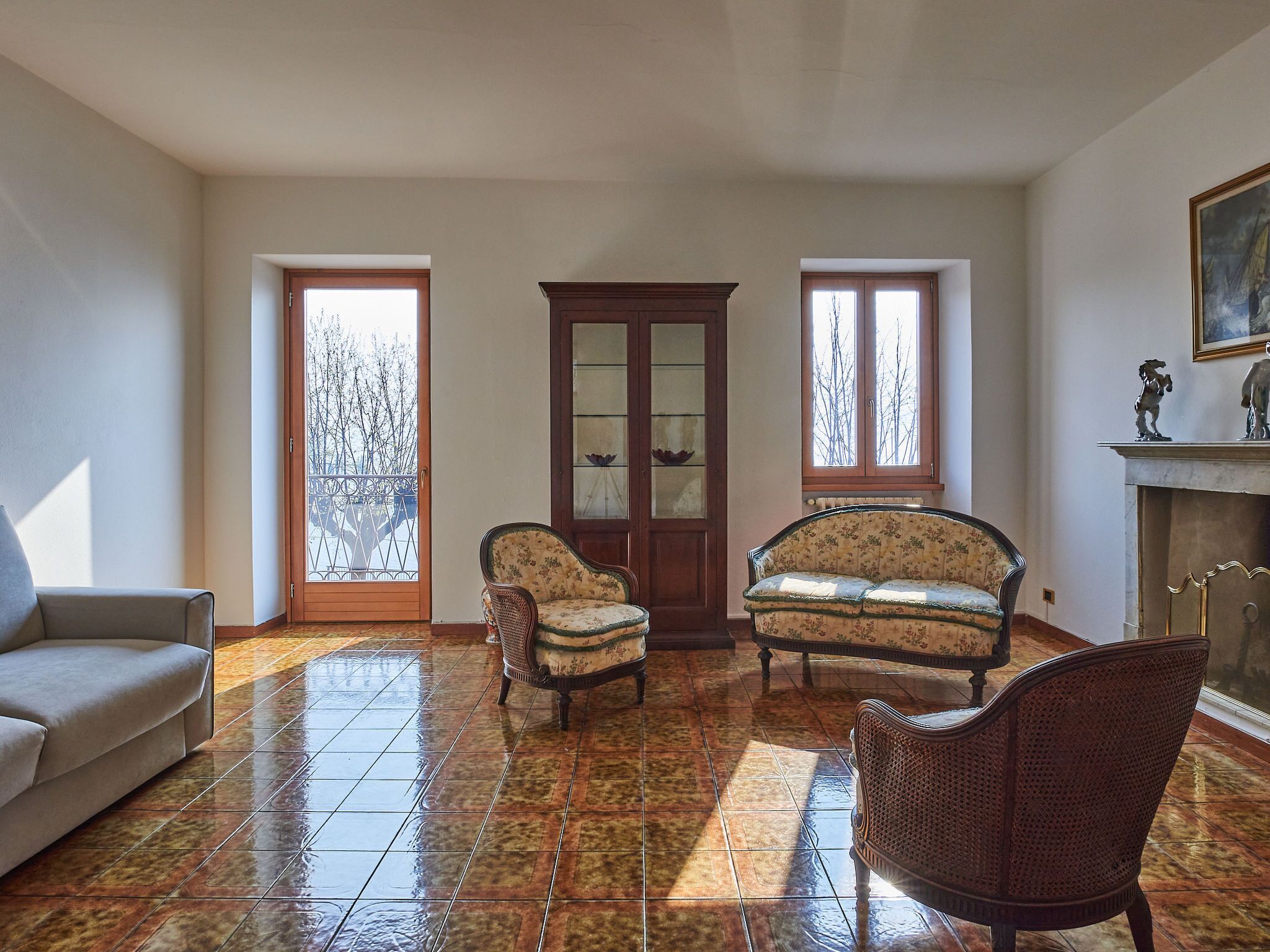 A spacious living room with a tiled floor, a sofa, two armchairs, and a cabinet.