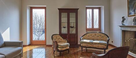 A spacious living room with a tiled floor, a sofa, two armchairs, and a cabinet.