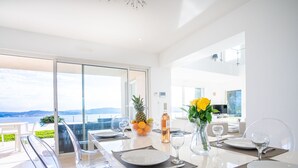 A modern dining area with a panoramic view, a glass table, and a vase with yellow flowers. - Lei Suve by Interhome (Grimaud)