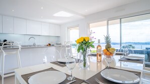 A modern dining area with a large table set for two, a kitchen in the background, and a view of the sea through large windows. - Lei Suve by Interhome (Grimaud)