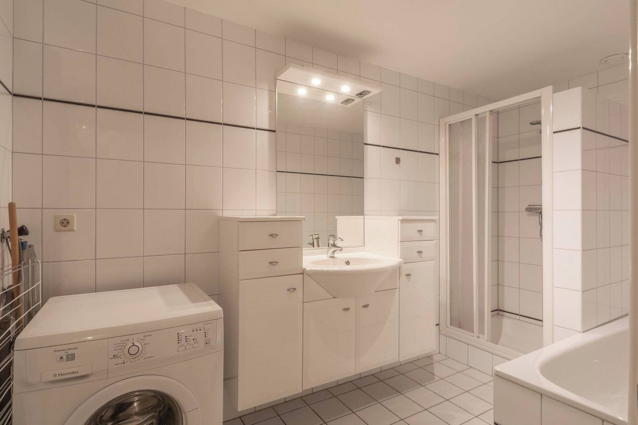 A modern bathroom with a washing machine, a sink, and a shower area.