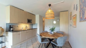 Una cocina moderna con armarios de madera clara, una isla central y una zona de comedor con mesa de madera y sillas grises.