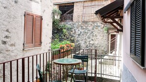 A narrow courtyard with a stone wall, a small table with chairs, and a decorative lantern. - Ludovica by Interhome (Dongo)
