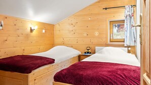 Ein gemütliches Holzhütten-Zimmer mit zwei Betten, jeweils mit einer roten Decke, einem kleinen Tisch mit einem Teddybären und einem Fenster mit Vorhängen.