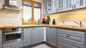 Eine moderne Küche mit grauen Schränken, einem Edelstahlbackofen, einer Kaffeemaschine und einem Fenster mit Vorhängen.