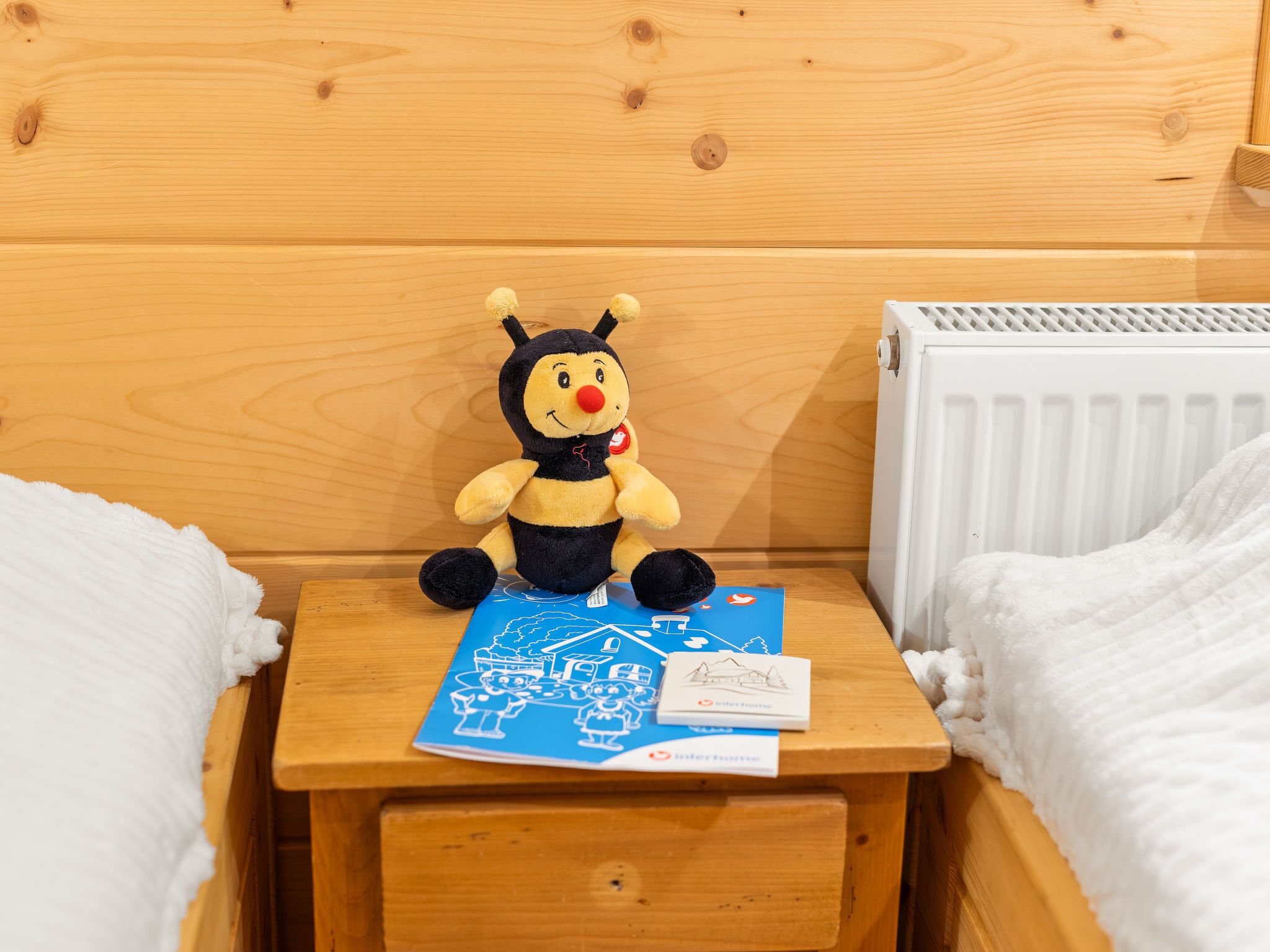 Ein Nachttisch aus Holz mit einem Stofftier, einem blauen Buch und einem weißen Kissen.