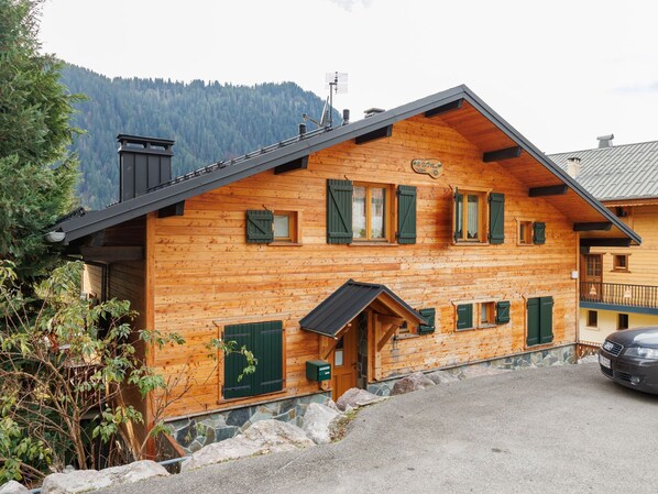 A wooden chalet with a sloped roof, multiple windows with shutters, and a stone foundation. - Fer à Cheval by Interhome (Châtel)