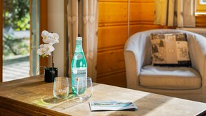 Una mesa de madera con una botella de agua Pellegrino, dos vasos, una orquídea en maceta pequeña y una revista.
