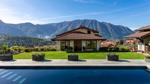 Une maison avec une piscine, entourée de montagnes et de verdure.