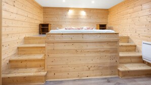 Eine Holzhütte mit einem Bett über einer Treppe, einem kleinen Regal und einem weißen Heizkörper.