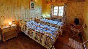 Puinen mökkimainen makuuhuone, jossa on kaksi sänkyä, yöpöytä, televisio ja ikkuna, jossa on verhot.