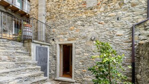 A stone building with a wooden staircase leading to a door, a potted plant, and a metal railing.