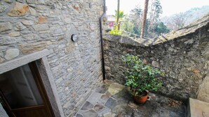 A stone-walled outdoor area with a potted plant, a window, and a stone floor.