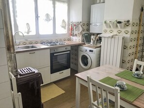 Une cuisine compacte équipée d’une cuisinière à gaz, d’un four, d’un lave-linge et d’un coin repas avec une table et des chaises.