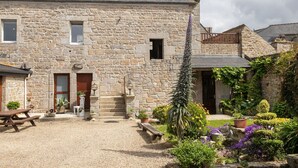 Un bâtiment en pierre avec une cour en gravier, des bancs en bois et des plantes en pot.