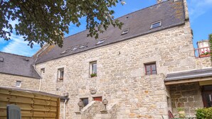 Un bâtiment en pierre avec une cour, un banc en bois et des plantes en pot.