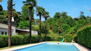 A swimming pool with a slide, surrounded by palm trees and a hilly landscape.