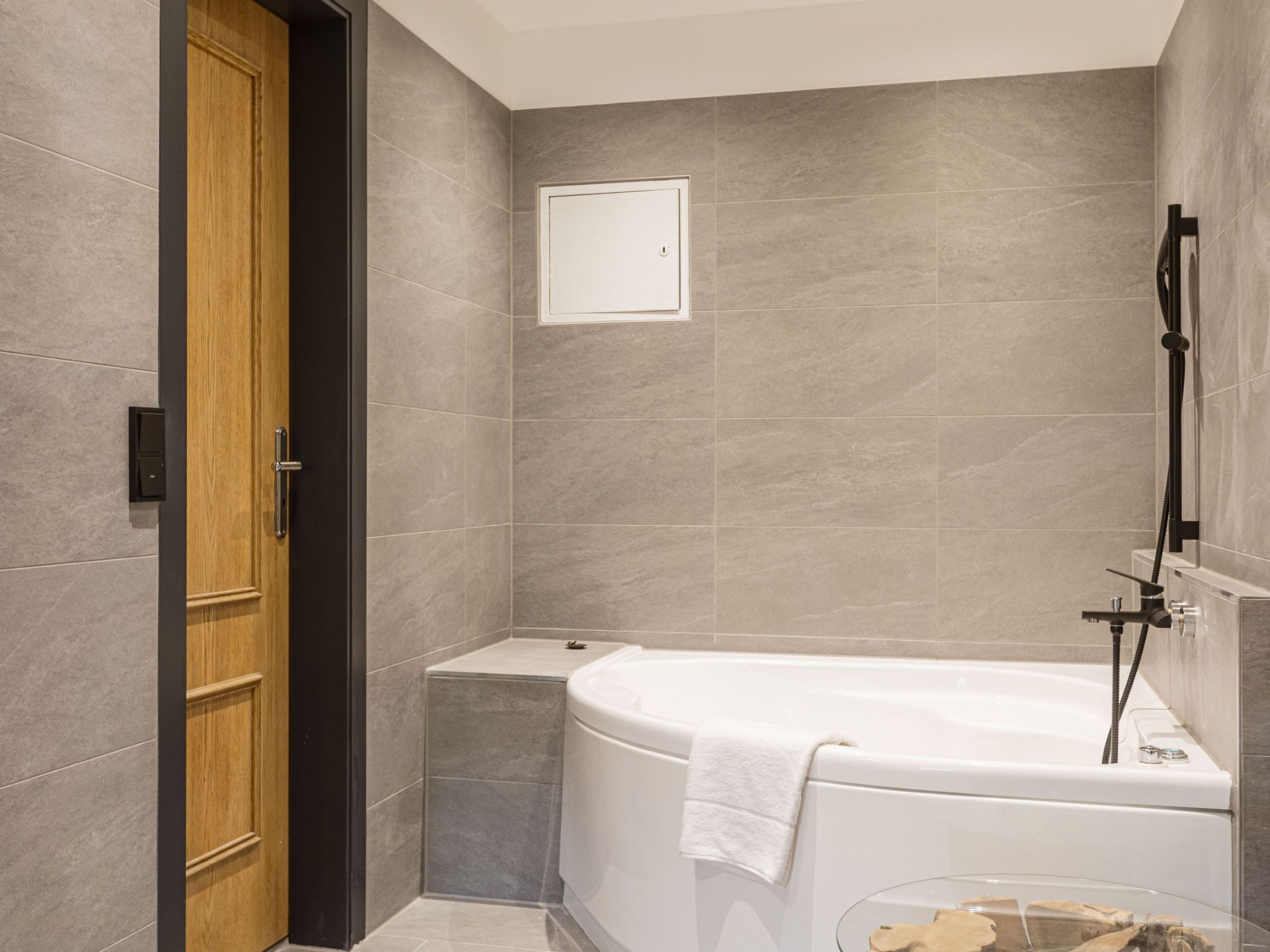 A modern bathroom with a bathtub, a wooden door, and a small shelf.