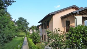 Un bâtiment à deux étages doté d’un balcon, entouré d’un espace verdoyant bien entretenu et bordé d’un chemin pavé.
