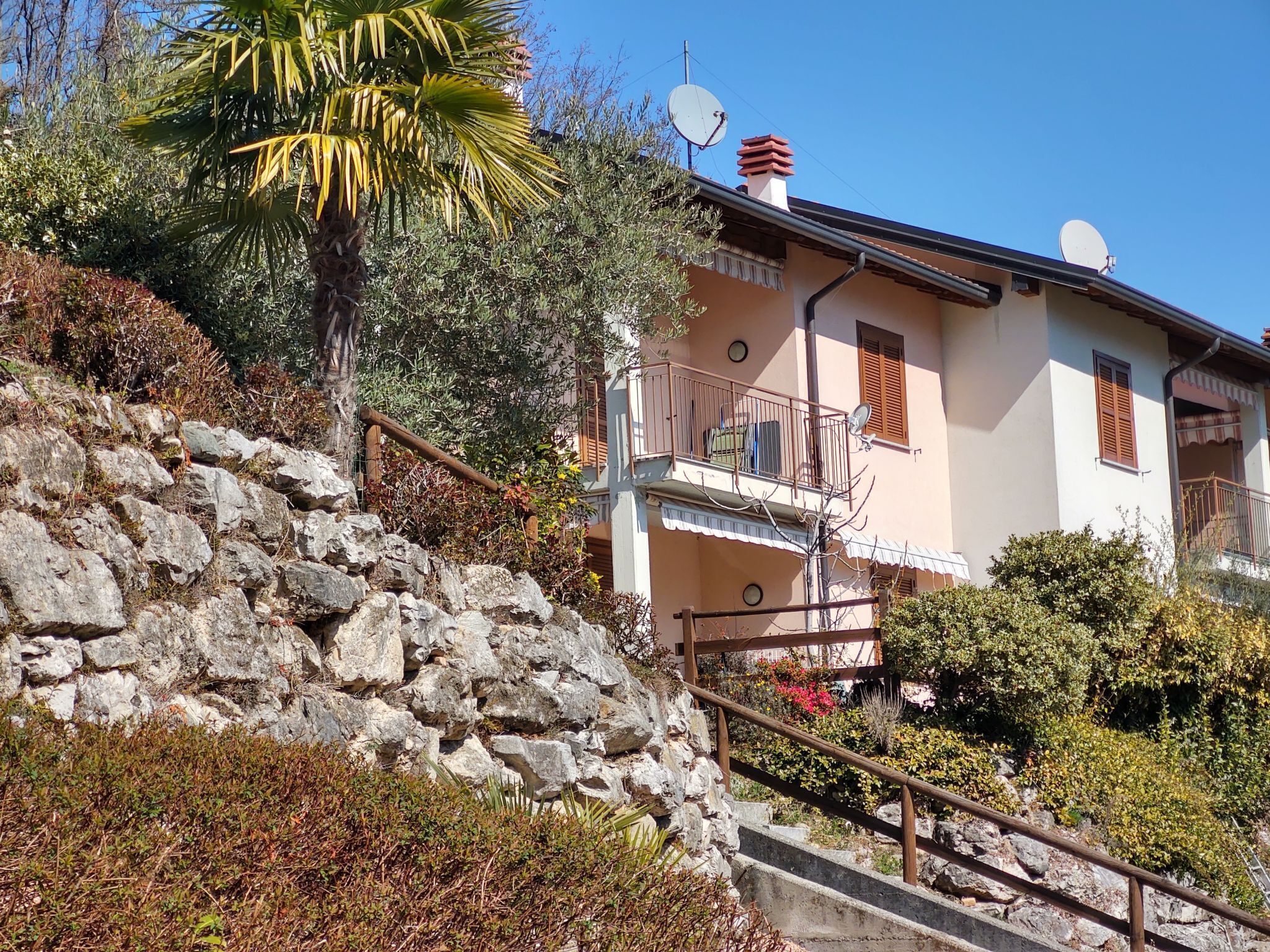 A stone staircase leading to a building with a balcony, surrounded by vegetation and a clear sky.
