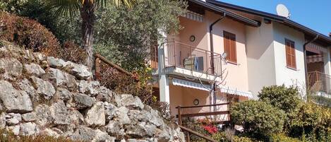 A stone staircase leading to a building with a balcony, surrounded by vegetation and a clear sky.