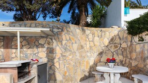 An outdoor patio with stone walls, a barbecue grill, and a round table with a vase of flowers.