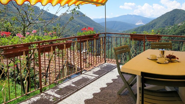 Eine Terrasse mit Tisch und Stühlen, einem Geländer und Blick auf Berge.