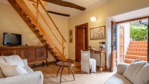 Un salón con escalera de madera, televisor, aparador, sofá y una mesa con un jarrón.