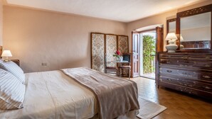 Un dormitorio con cama, cómoda, escritorio y silla, y una puerta que da a un balcón.