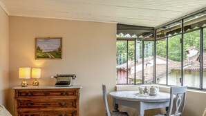 A cozy room with a wooden dresser, a desk with a typewriter, a round table with chairs, and a window with a view of a village. - Rachele by Interhome (Verbania)
