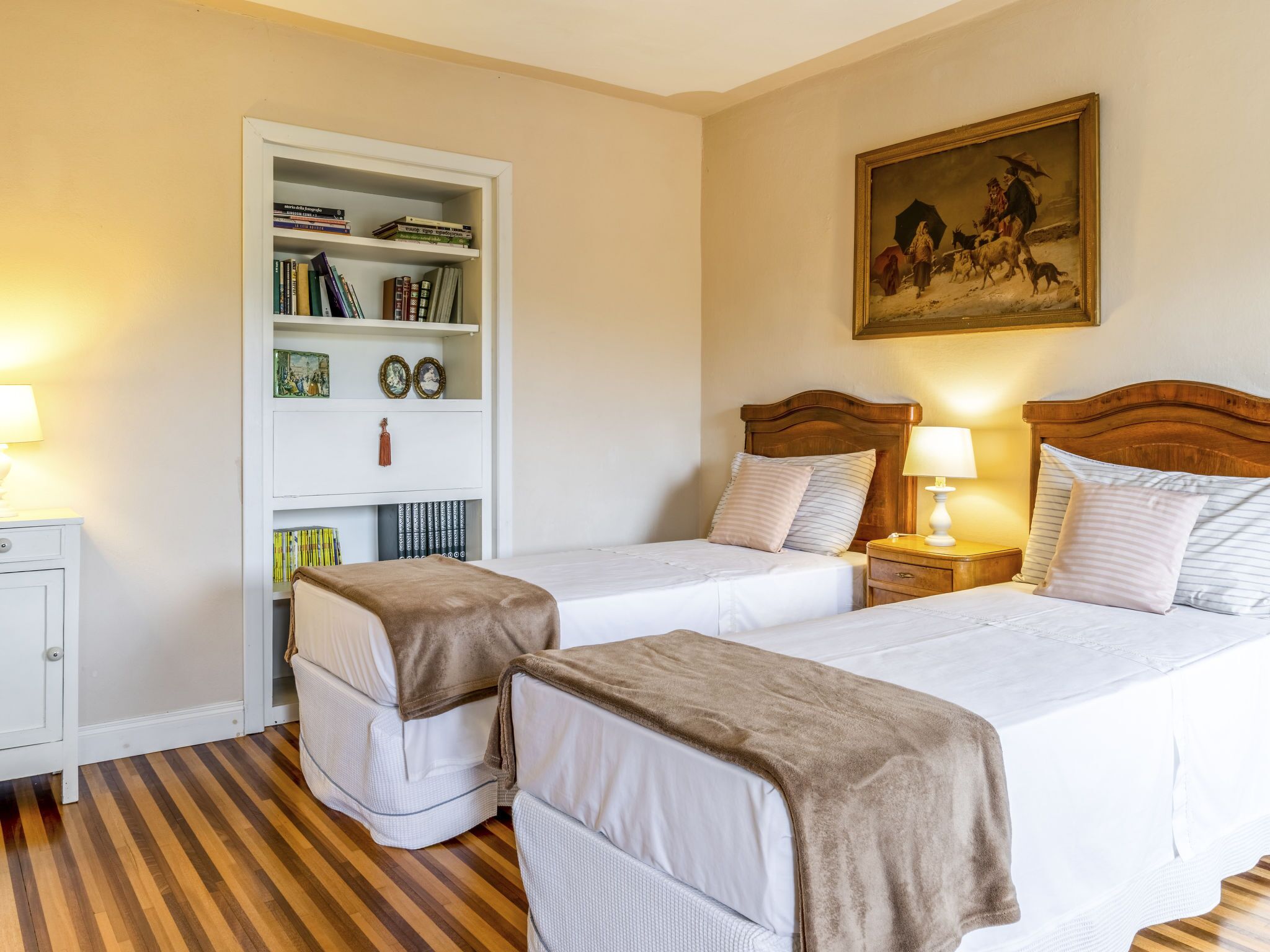 Una habitació d'hotel amb dos llits individuals, una estanteria, un quadre a la paret i un terra de fusta.