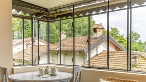A conservatory with a round table and chairs, a view of neighboring houses, and a window with metal bars. - Rachele by Interhome (Verbania)