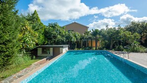 A swimming pool with a tiled edge, surrounded by lush greenery and a building in the background.