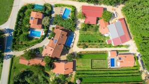 An aerial view of a residential area with multiple houses, each featuring a swimming pool and surrounded by greenery.
