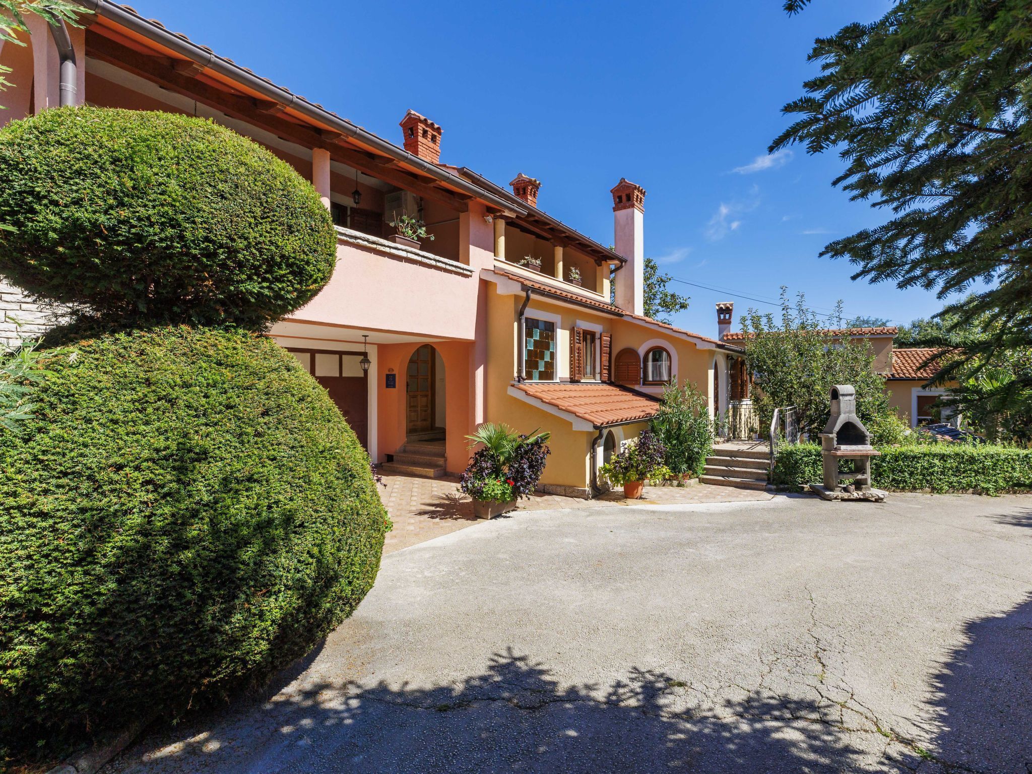 A two-story building with a red-tiled roof, a stone chimney, and a small garden area with a stone oven.