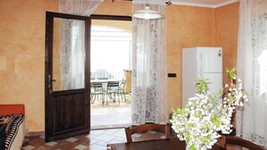 A dining area with a wooden table and chairs, a vase with flowers, a white refrigerator, and a view of an outdoor patio with a table and chairs. - Francesca (VGO210) by Interhome (Varigotti)