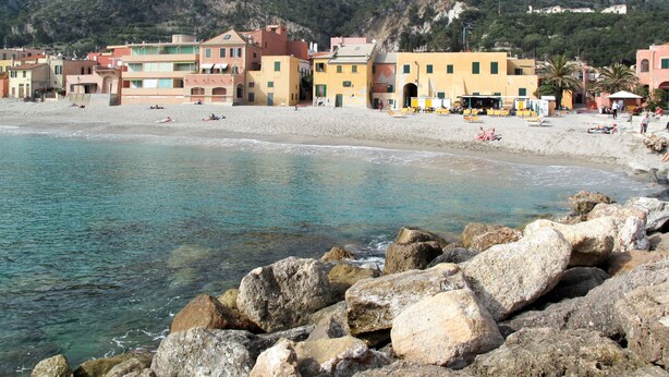 A coastal town with buildings along the beach and rocky shores in the foreground. - Francesca (VGO210) by Interhome (Varigotti)