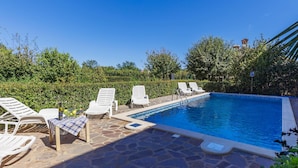 A swimming pool with white lounge chairs and a table with a bottle and glasses. - Vacation home Jakov by Interhome (Rovinj)
