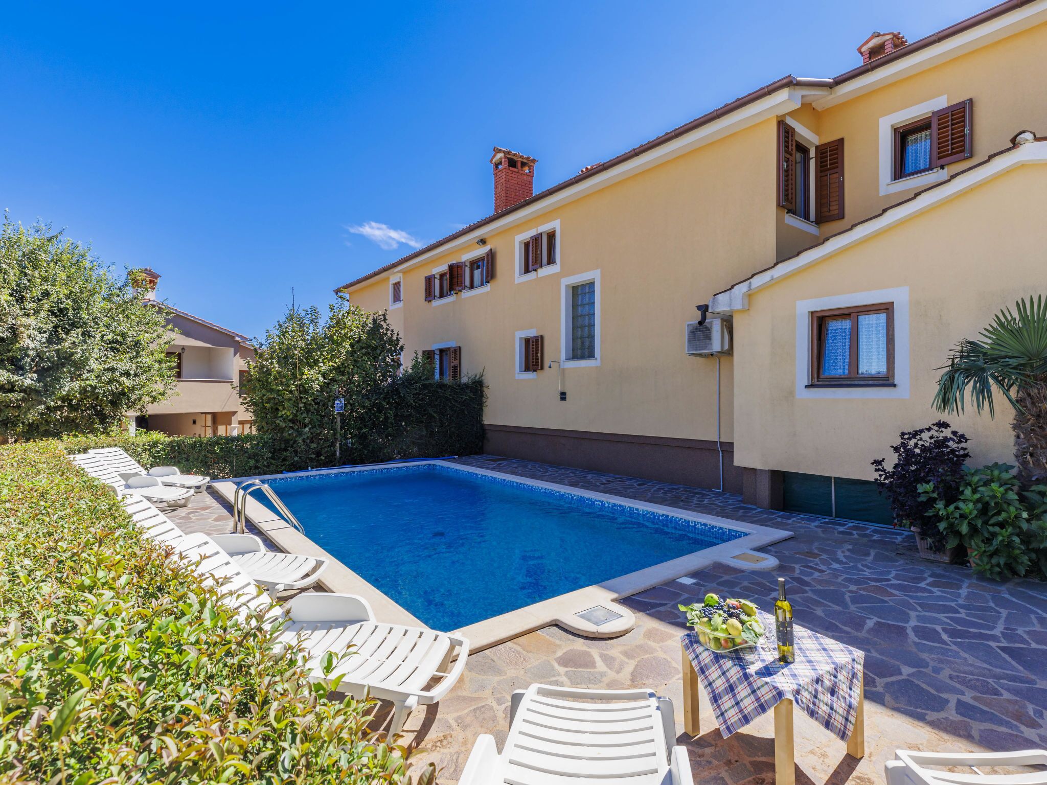 A poolside area with lounge chairs and a table with a bottle and fruit.