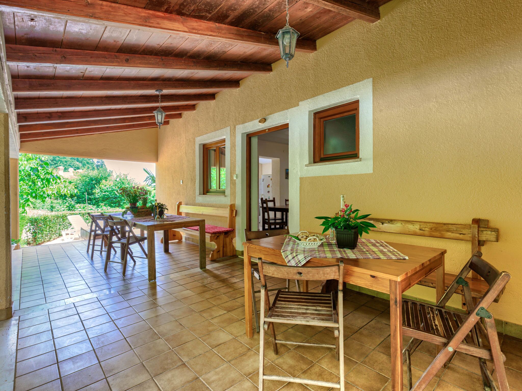A covered patio with wooden furniture, a bench, and a table with a bottle and plant.