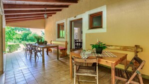 A covered patio with wooden furniture, a bench, and a table with a bottle and plant. - Vacation home Jakov by Interhome (Rovinj)