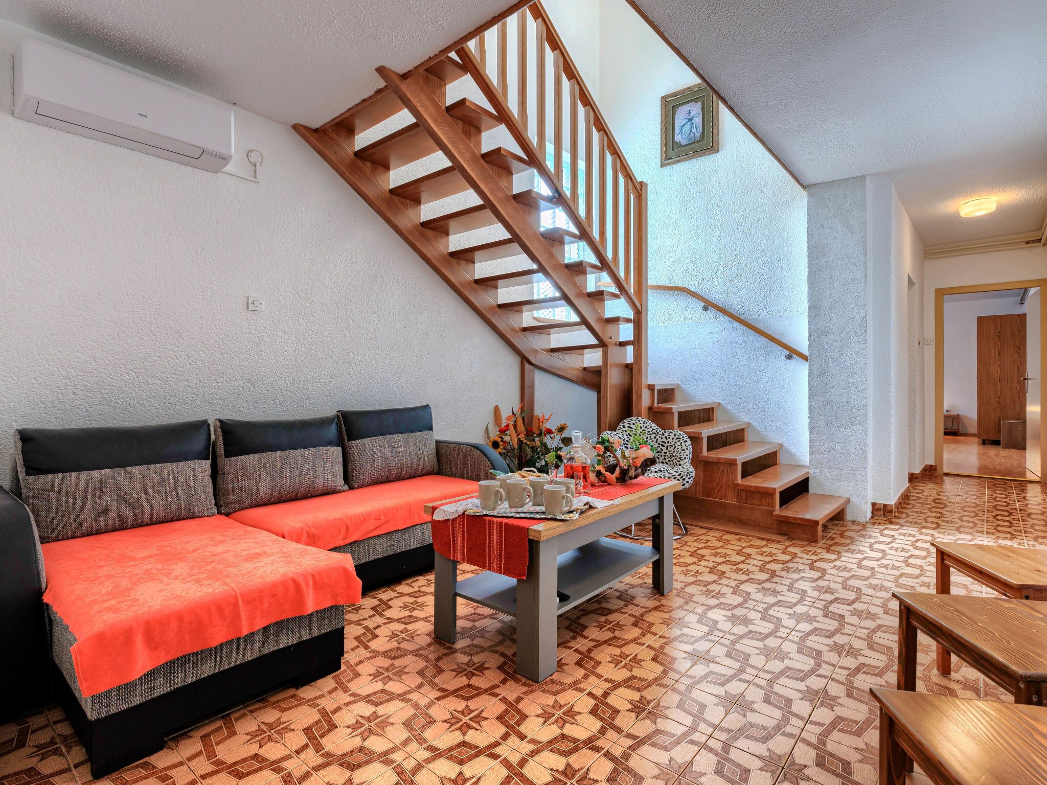 A living room with a sofa, coffee table, and patterned floor. A wooden staircase leads to another room.