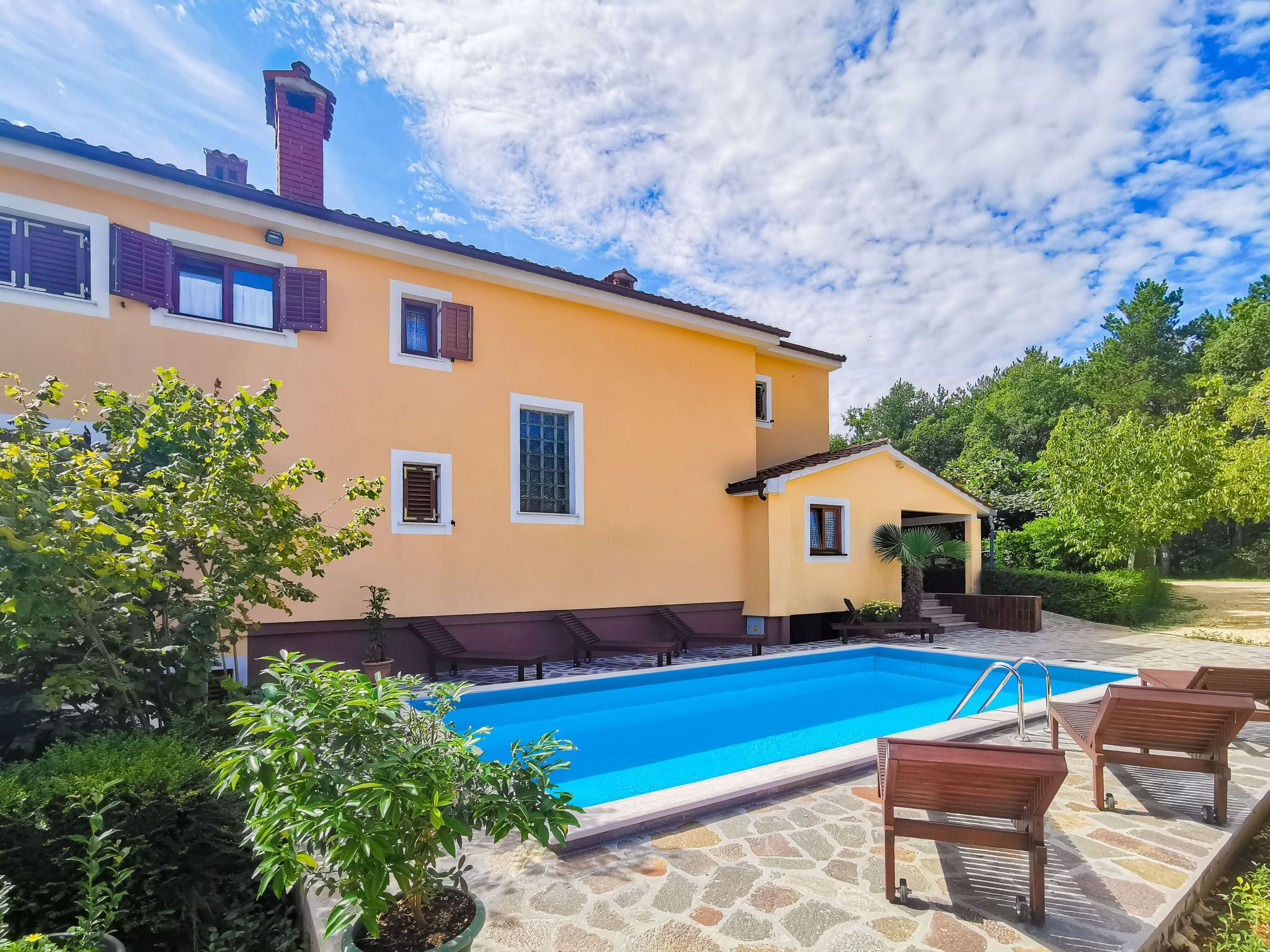 A two-story building with a swimming pool, outdoor seating, and a garden area.