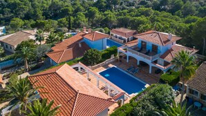 A large villa with a swimming pool, surrounded by lush greenery and a view of the sea.