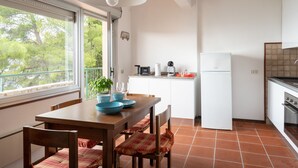 Een moderne keuken met witte kasten, een witte koelkast en een zwart aanrecht. Er staat een eettafel met blauwe kommen en een potplant.