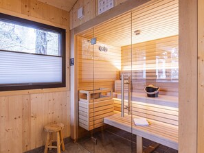 A sauna room with wooden walls, a bench, a stool, and a window.
