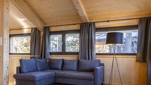 A wooden interior with a gray sofa, a floor lamp, and large windows with curtains.