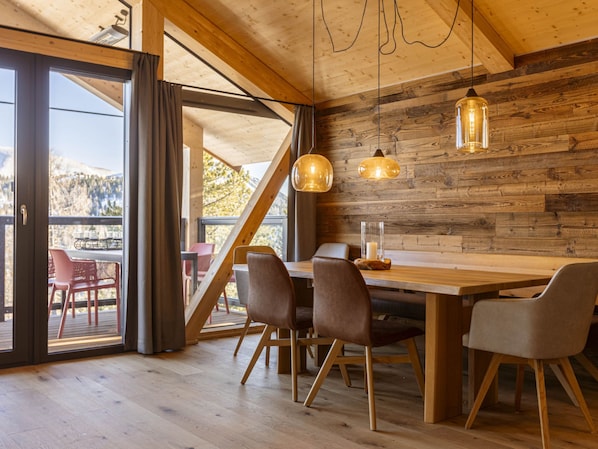 A wooden interior with a dining table, chairs, and pendant lights.