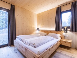 A wooden cabin bedroom with a bed, bedside lamps, and a window with curtains.